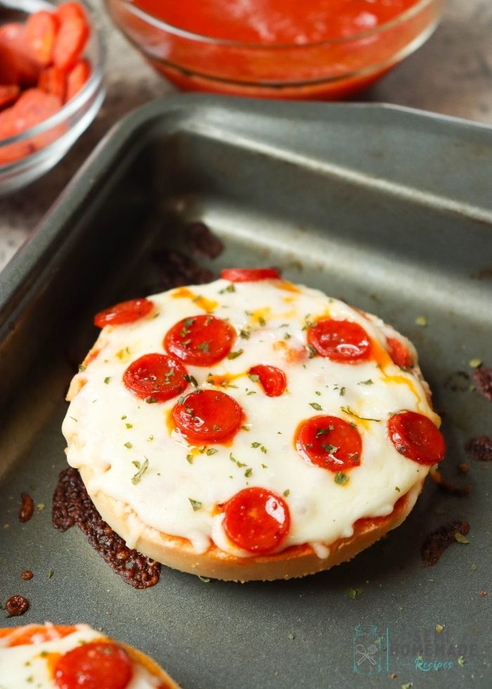 Mini pizza bagel on baking sheet with melted cheese and pepperoni
