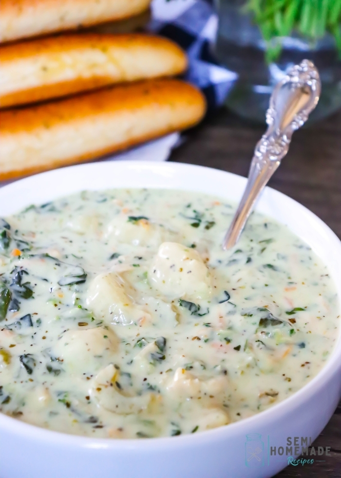 Better Than Olive Garden Chicken Gnocchi Soup in white bowl with breadsticks behind it (1)