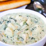 Better Than Olive Garden Chicken Gnocchi Soup in white bowl with breadsticks behind it