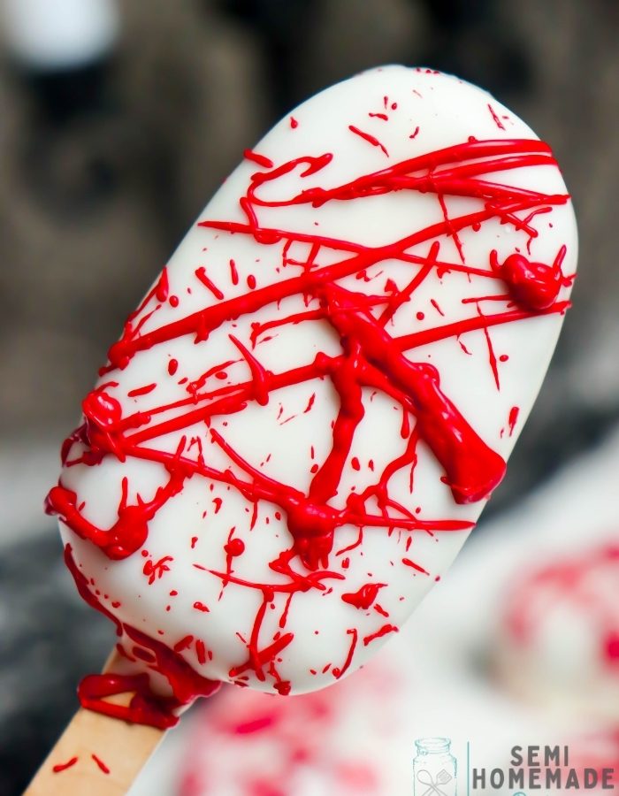 Blood Splatter Cakesicles made with red velvet cake and dipped in white chocolate candy coating, then decorated with red chocolate "blood splatter" for a creepy Halloween dessert!