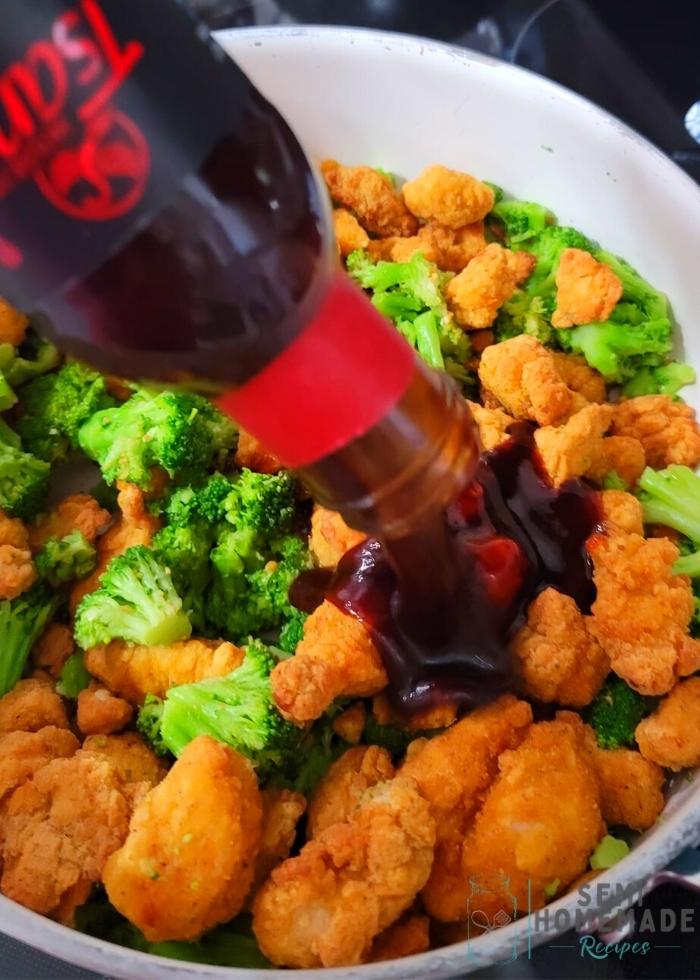 Pouring General Tso Sauce into Cooked Popcorn Chicken and Steamed Broccoli in Skillet