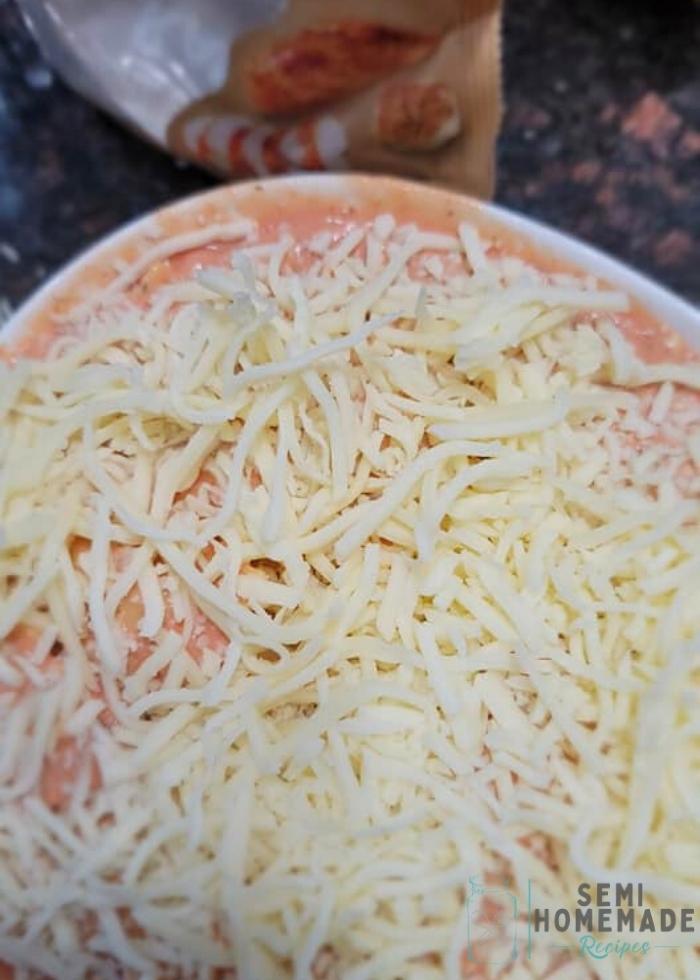 pink sauce mixed with pasta in casserole dish with shredded cheese