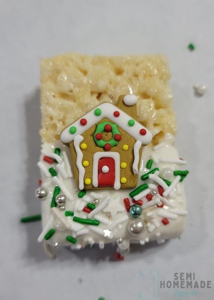 rice krispie treat half covered in white chocolate with royal icing gingerbread house in middle with sprinkles