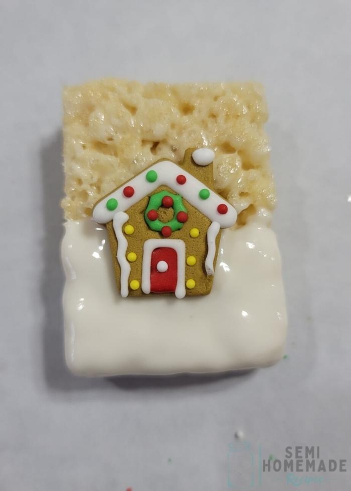 rice krispie treat half covered in white chocolate with royal icing gingerbread house in middle