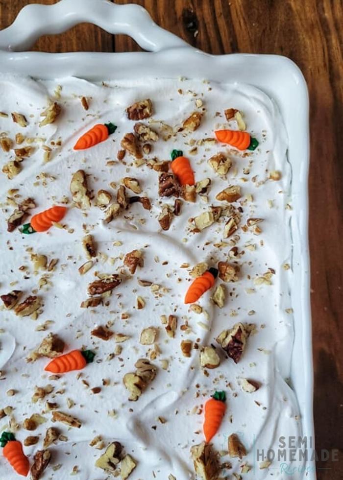 CARROT CAKE POKE CAKE with royal icing carrots on top of whipped cream with chopped pecans