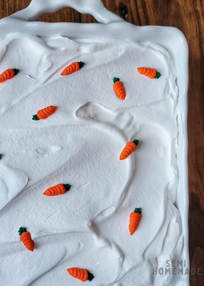 CARROT CAKE POKE CAKE with royal icing carrots on top of whipped cream