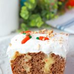 Slice of CARROT CAKE POKE CAKE on white plate with green in the background
