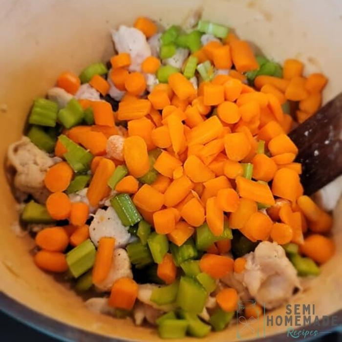 chopped carrots and chopped celery and chicken in a pot