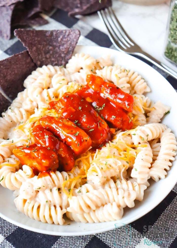 Grilled Chicken tossed in BBQ sauce, on top of cajun sauce coated fusilli pasta and cheese on a white plate.