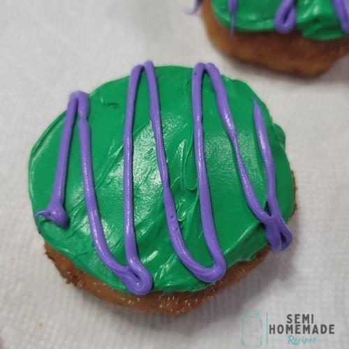 fried biscuit donut covered in green frosting, purple frosting swiggles