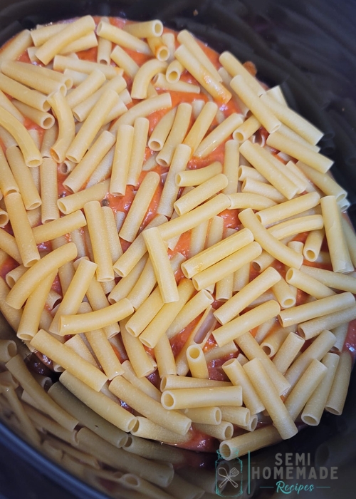 dry pasta in bowl of slow cooker with pasta sauce